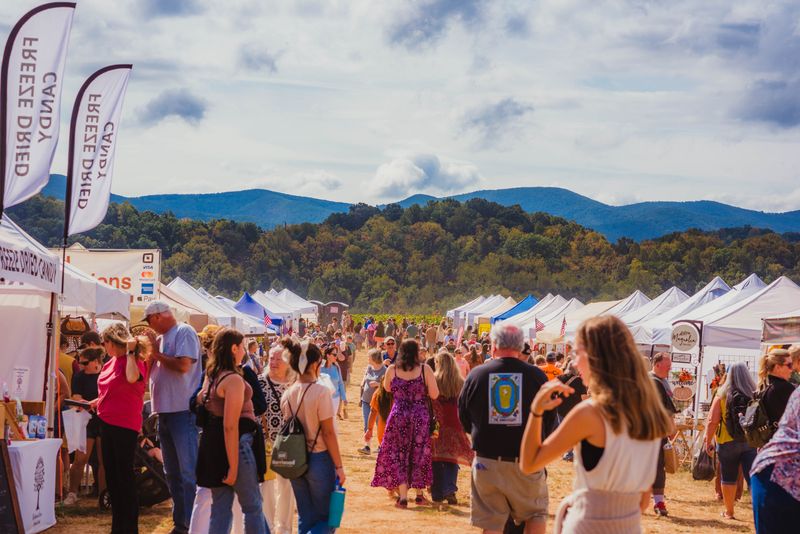 Crowds stroll the vendor tent rows at the Beaver Dam Farm Sunflower Festival with the Blue Ridge Mountains behind.