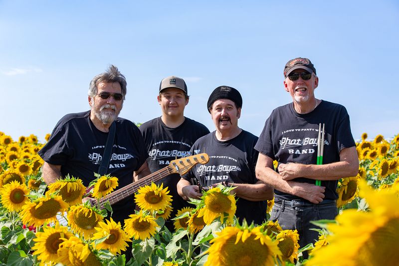 Members of the Phat Boys Band pose with a guitar among blooming sunflowers.